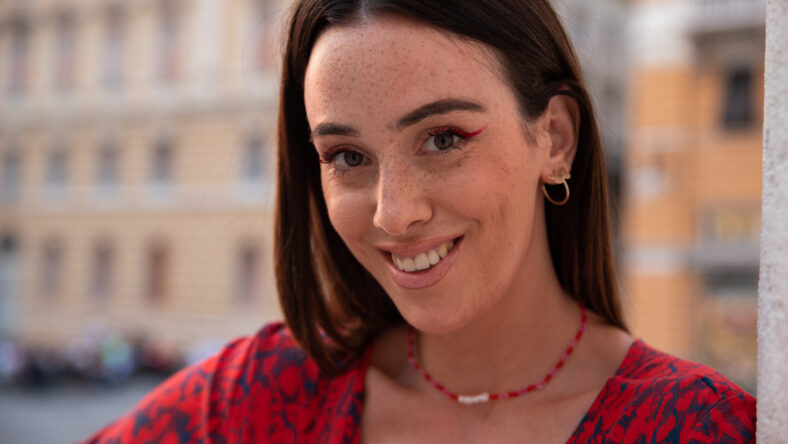 Young girl with freckles smiles outside in downtown looking confidently ahead.