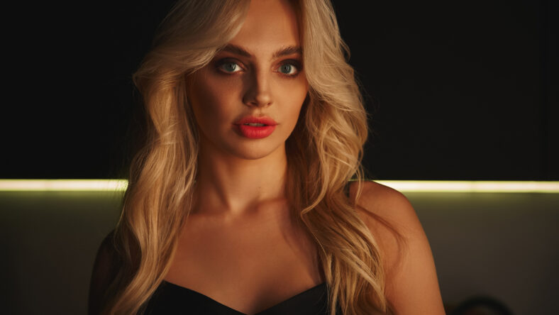 appealing blonde woman in black dress with smokey eyes posing and looking straight at camera