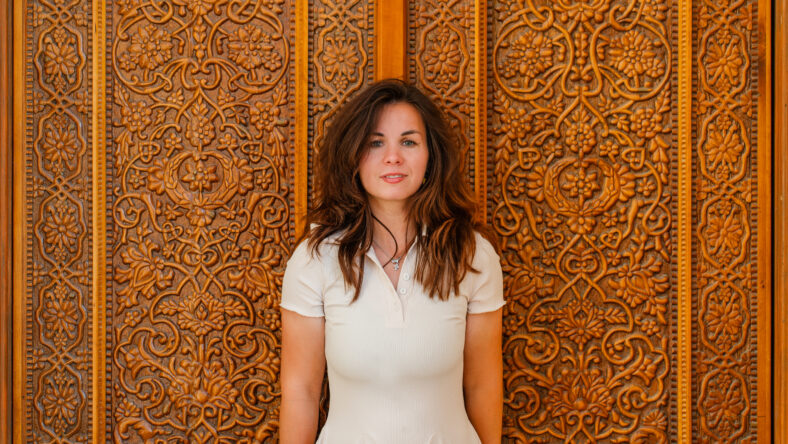 Portrait of a young woman standing at a beautiful carved wooden door.