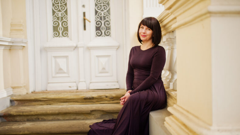 Adult brunette woman at violet gown background old vintage house with stairs.
