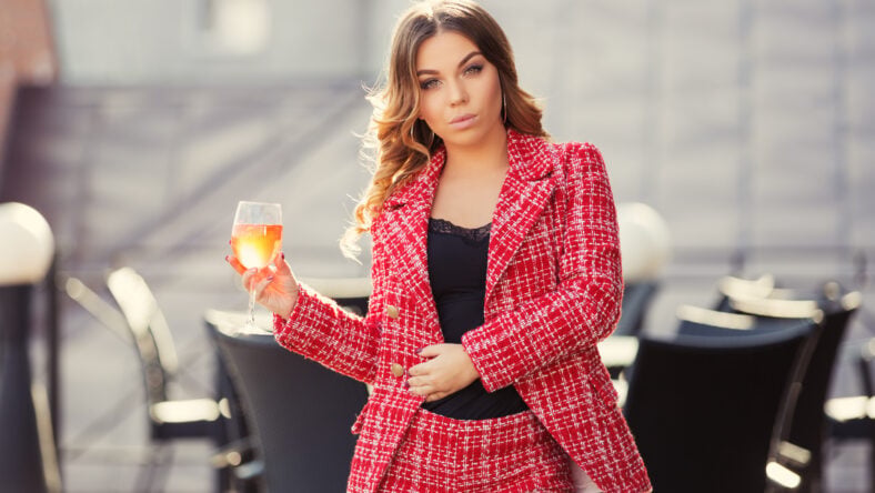 Young fashion woman with long curly hairs at sidewalk cafe Stylish female model wearing red tweed jacket and shorts suit