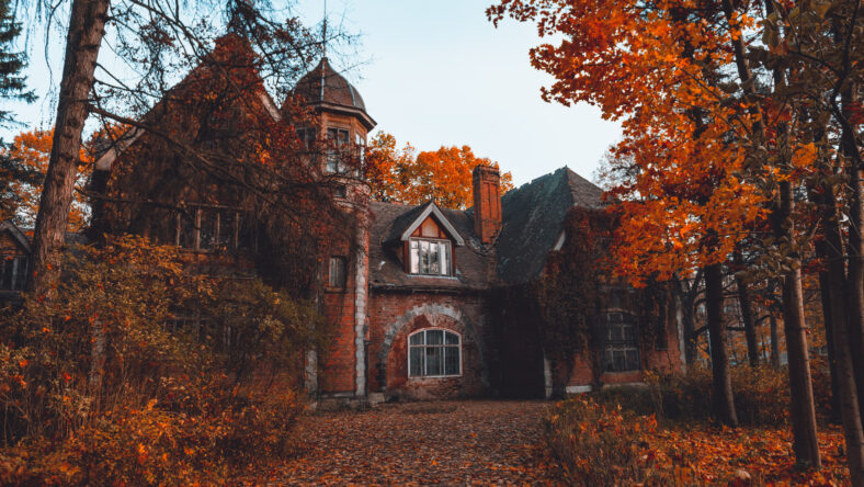 Manor house with trees in autumn colors and fall trees. Old Victorian Haunted House long abandoned to the ghosts. Abandoned house in autumn wood.