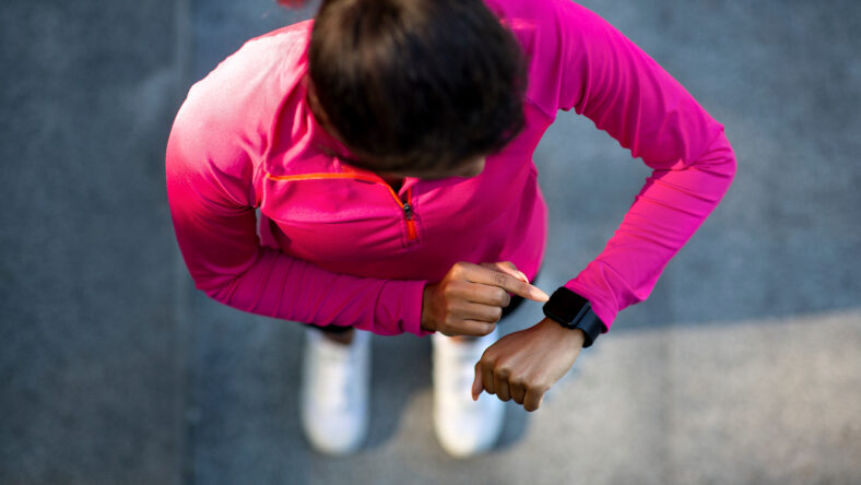 Top view on african american woman in sportswear looking at smartwatch, checking her pulse while training at park