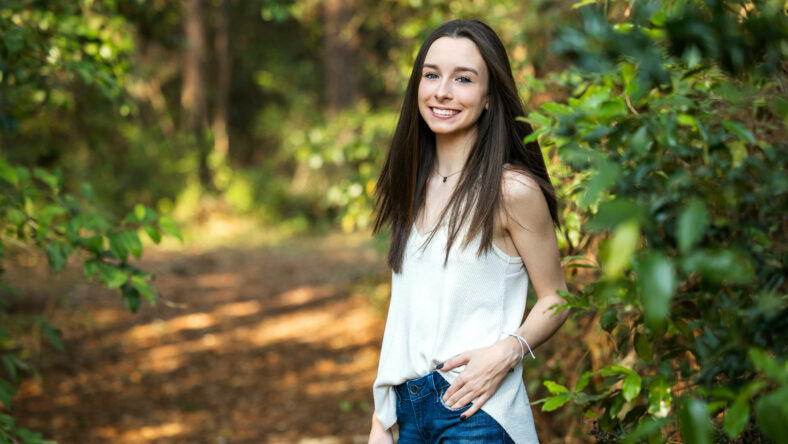 A beautiful happy teenage brunette girl outdoors in a wooded area in the spring.