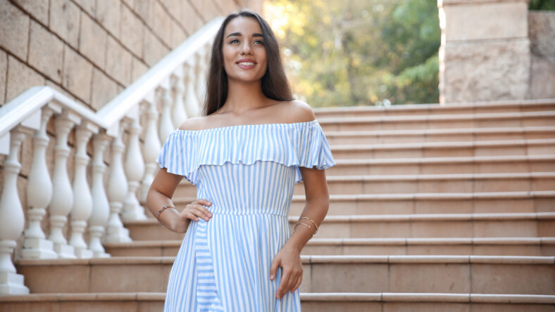 Beautiful young woman in stylish light blue striped dress on stairs outdoors