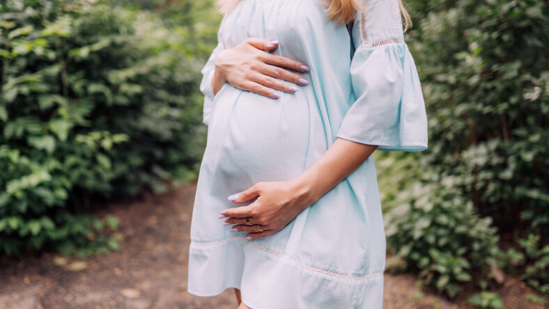 Close up of pregnant belly in nature. Pregnant girl in the sunset, pregnant woman relaxing outside in the park