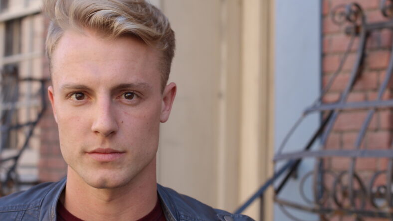 close portrait of handsome adult blonde man, with blured urban classic background