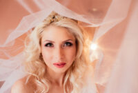 Beautiful emotional blonde bride posing under veil,