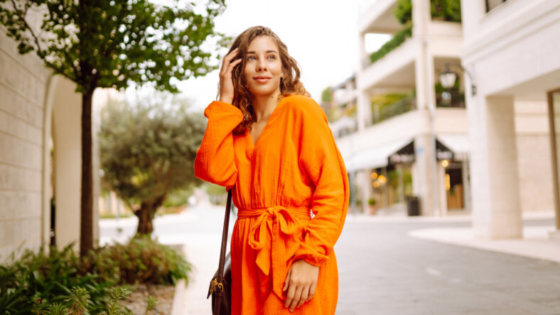Cheerful tourist in a bright dress walks along a beautiful street. A young woman enjoys the weather outdoors. The concept of walking, vacation, travel. Active lifestyle.