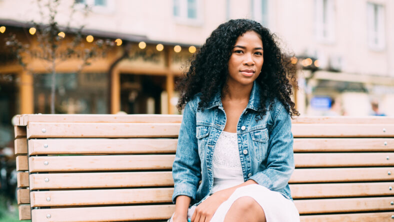 Portrait of yyoung african american woman with afro hairstyle sitting on the wooden bench outdoor.