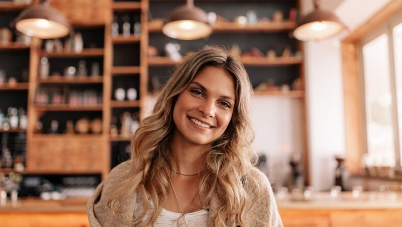 Portrait of beautiful young woman standing in a coffee shop. Young caucasian female in a cafe looking at camera and smiling.