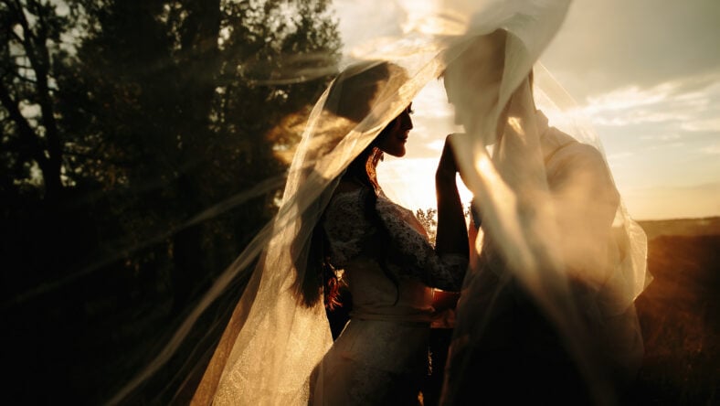 Beautiful wedding couple portrait behind veil. Sunrise