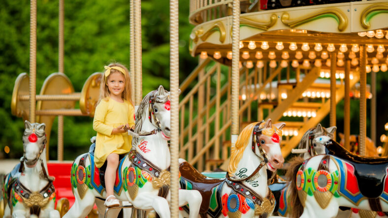 Adorable little girl near the carousel outdoors in Paris, baby girl on the carousel, Happy healthy baby child having fun outdoors on sunny day. Family weekend or vacations