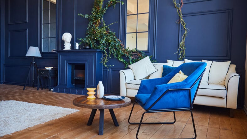 Modern interior with a fireplace, a spacious living room with blue walls and wooden floors, a blue armchair in the foreground and a white sofa against the wall. The concept of art Nouveau style, a real photo of the interior.