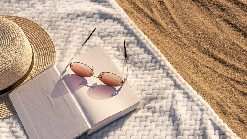 Summer vacation on the beach on the sand. On a white towel, a book and a hat and glasses. Close-up.