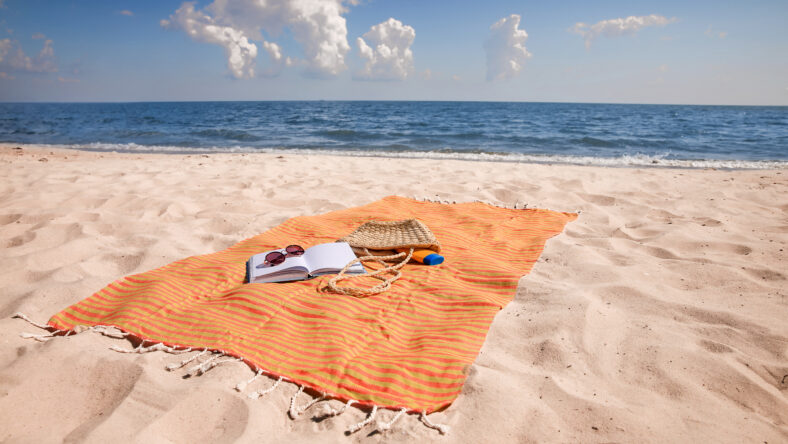 Orange striped beach towel with bag, accessories and book on sandy seashore