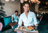 Beautiful young waitress serving delicious burger to