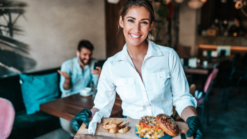 Beautiful young waitress serving delicious burger to