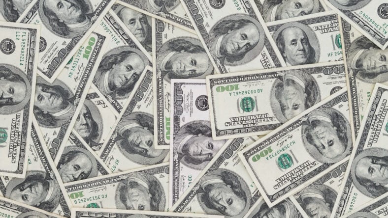 Hundreds of new Benjamin Franklin 100 dollar bills arranged randomly with the portrait facing uppermost in a closeup conceptual financial and monetary background
