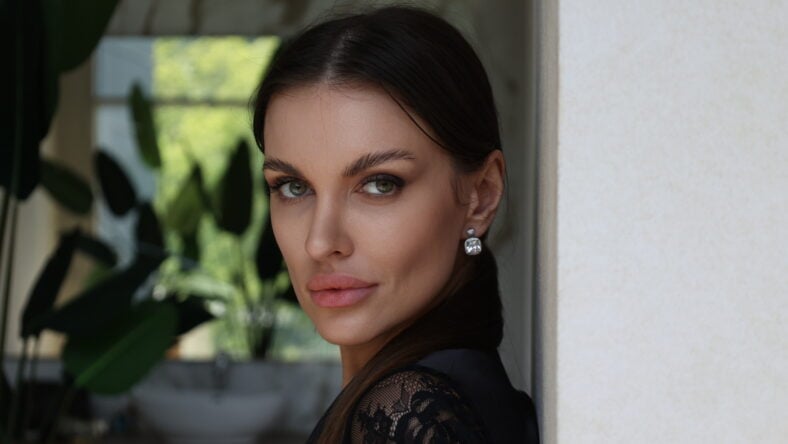 Beautiful brunette woman portrait smile. Portrait of young pretty woman in black night gown in her bathroom. Closeup, big lips. Plants, wooden table.