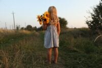 Little girl with sunflowers at meadow, back