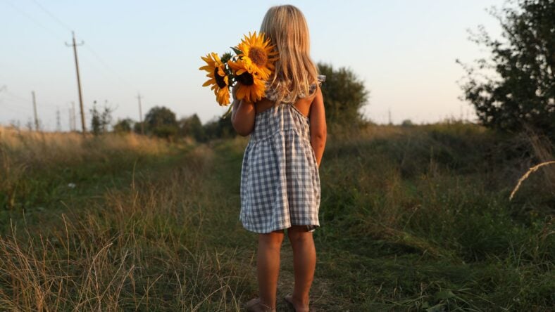 Little girl with sunflowers at meadow, back