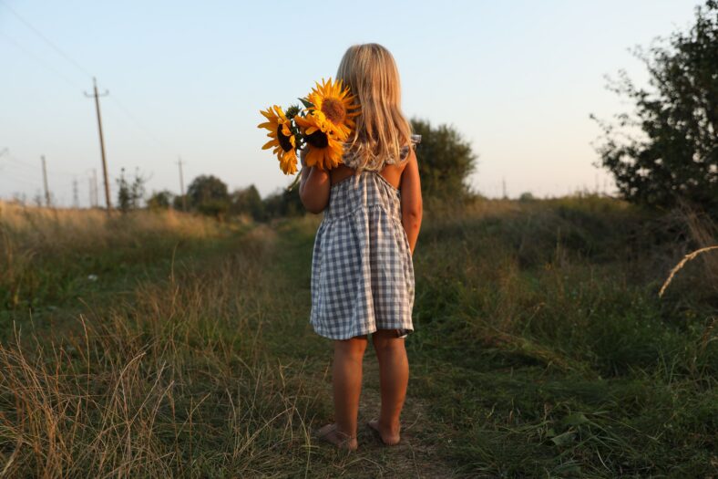 Little girl with sunflowers at meadow, back