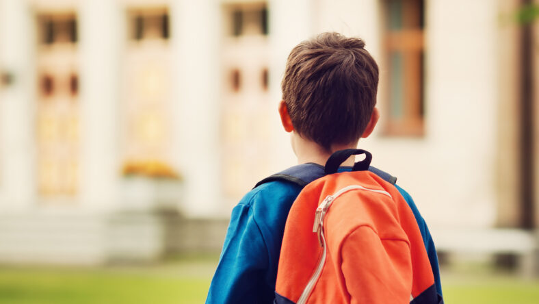 Boy with rucksack infront of a school