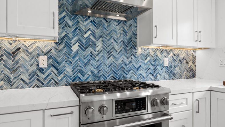Modern white kitchen with blue tile backsplash, stainless steel appliances, and minimalist cabinetry