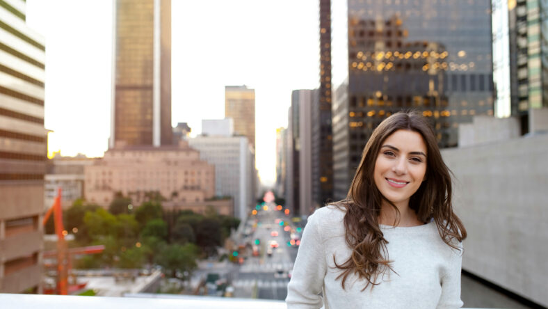 Beautiful young woman sitting on a bridge across the boulevard in urban scenery, downtown, at sunsetm smiling spontaneous.