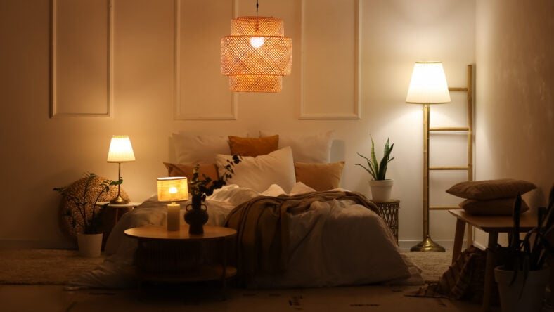 Interior of stylish bedroom with cozy bed, houseplants and glowing lamps at night