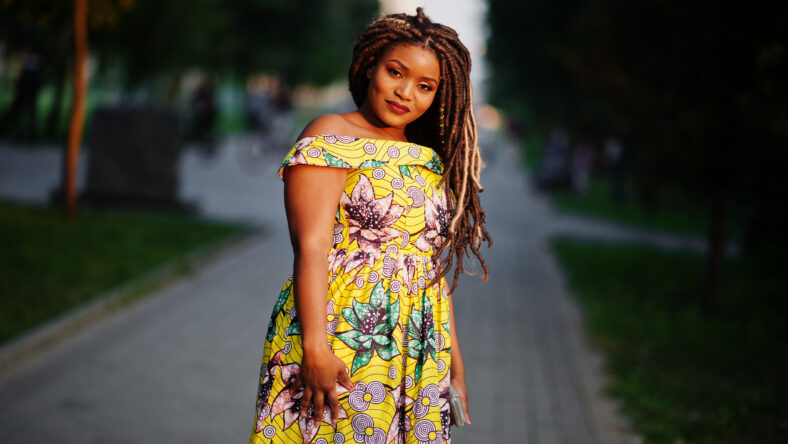 Cute small height african american girl with dreadlocks, wear at coloured yellow dress, posed at sunset.