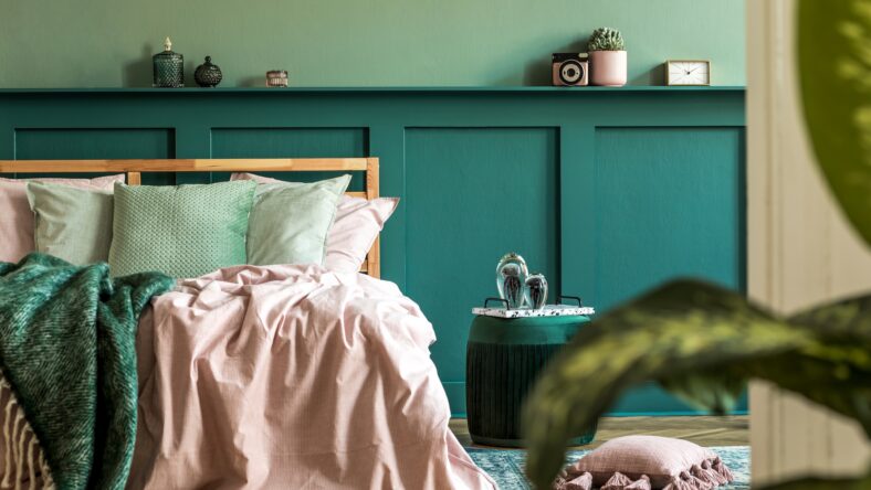 Stylish interior design of bedroom with modern furnitures, plants and elegant accessories. Shelf above the bed. Beautiful pink and green bed sheets, blankets and pillows. Modern home decor. Template.
