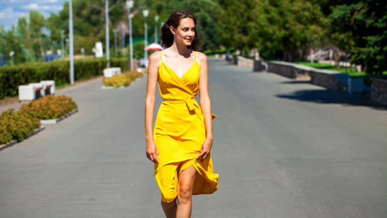 close up portrait of a young blonde woman in yellow dress walking in summer park