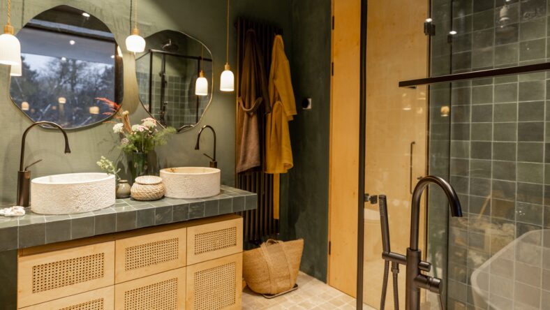 Bathroom interior with stone wash basins, modern faucets, irregularly shaped mirrors and wooden rattan commode in green and beige tones in natural boho style