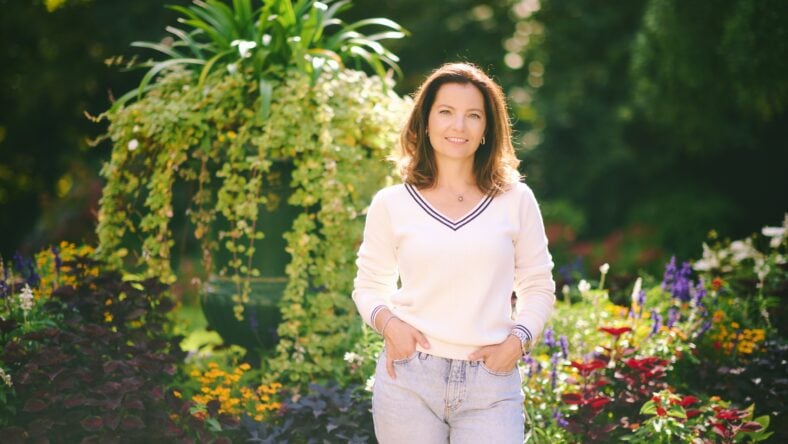 Outdoor portrait of happy beautiful 40 - 45 year old woman, wearing white pullover, posing in park on a very sunny day, healthy lifestyle