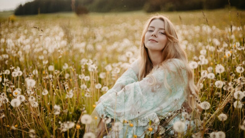 young woman in a dress in a dandelion field at sunset, the concept of the onset of summer, vacation dreams and memories.